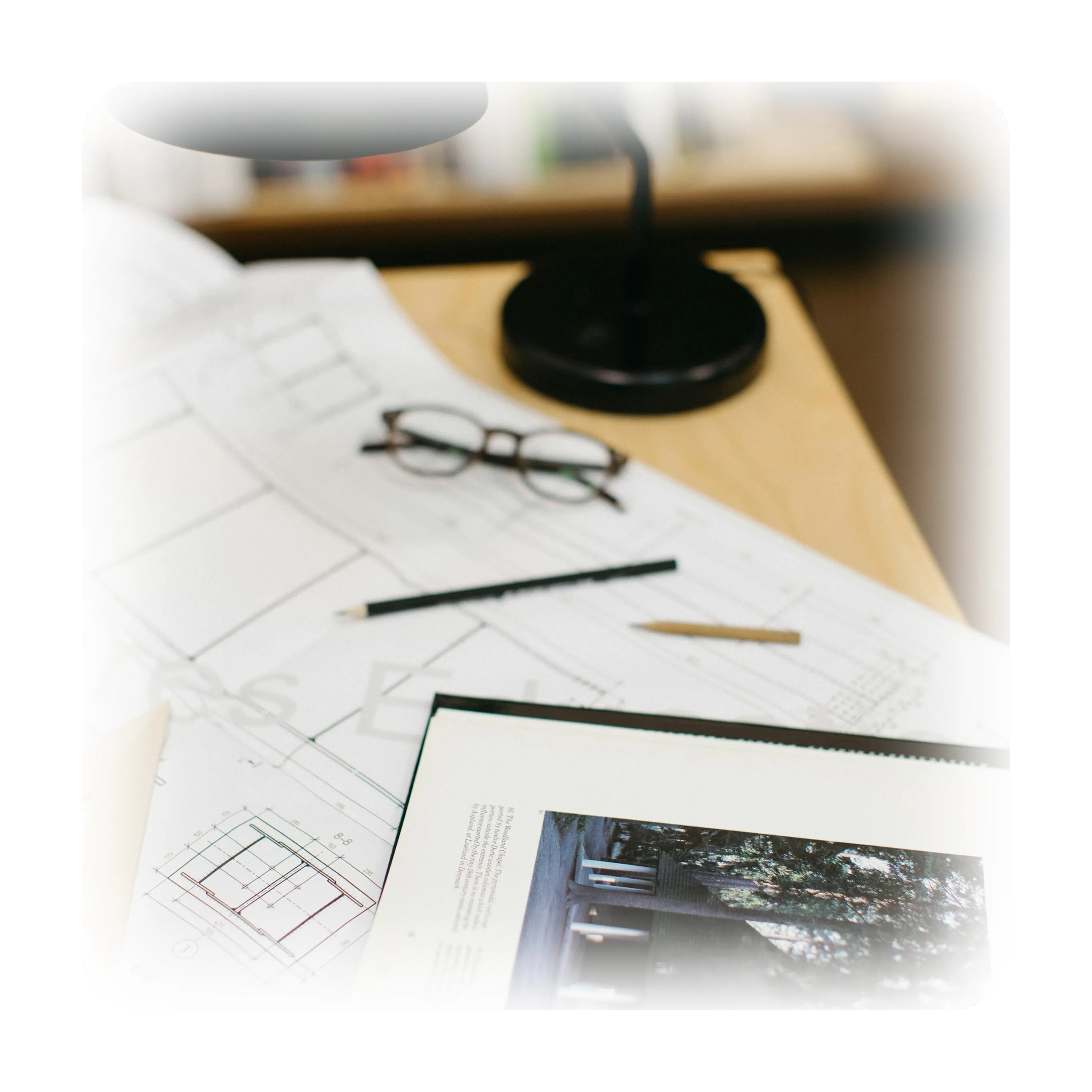 A creative workspace featuring architectural blueprints, sketches, and pencils laid out on a wooden desk under a desk lamp.